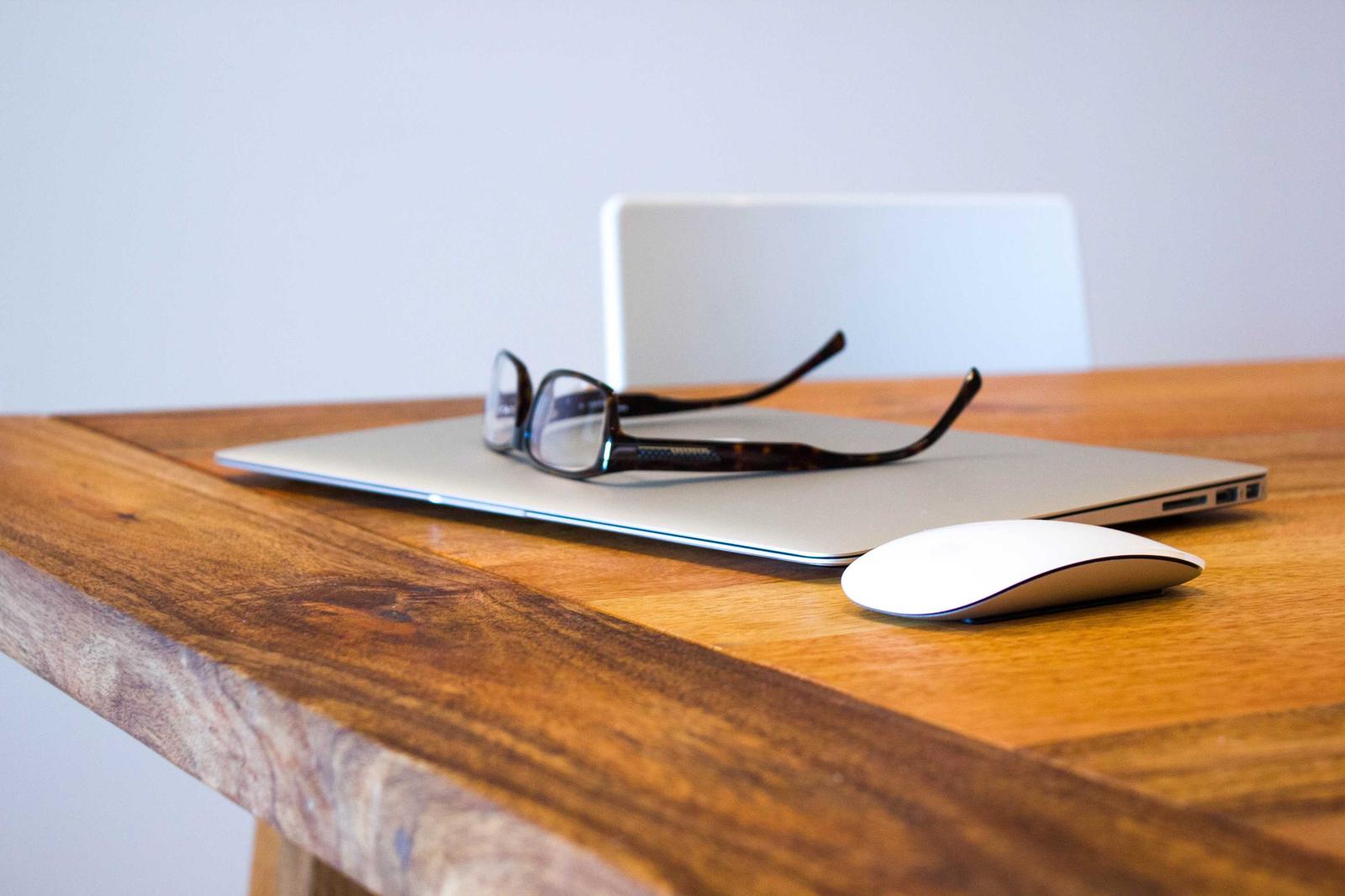 A thick wooden desktop with a live grain edge, a closed laptop, glasses and a mouse on it